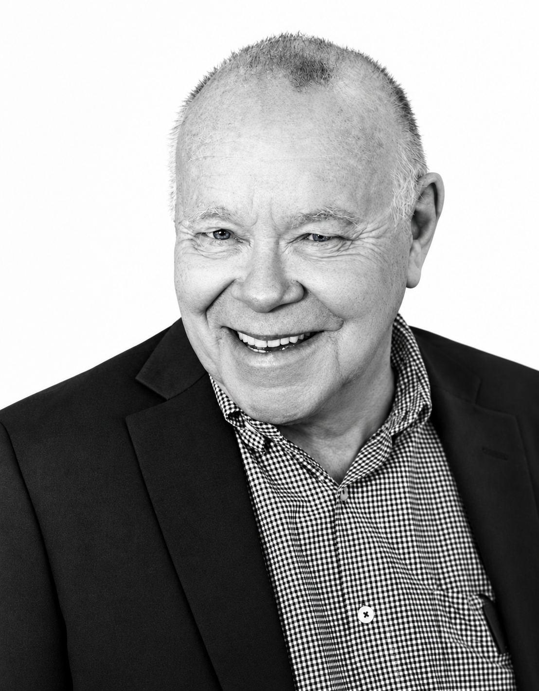Svartvitt porträtt på Anders, en äldre leende man i mörk kavaj och rutig skjorta.